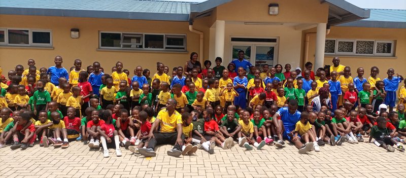 A large group of children in coloured sports shirts gathered outside a school building